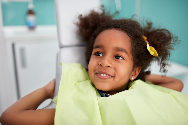 A young girl sits in a dental exam chair after a checkup