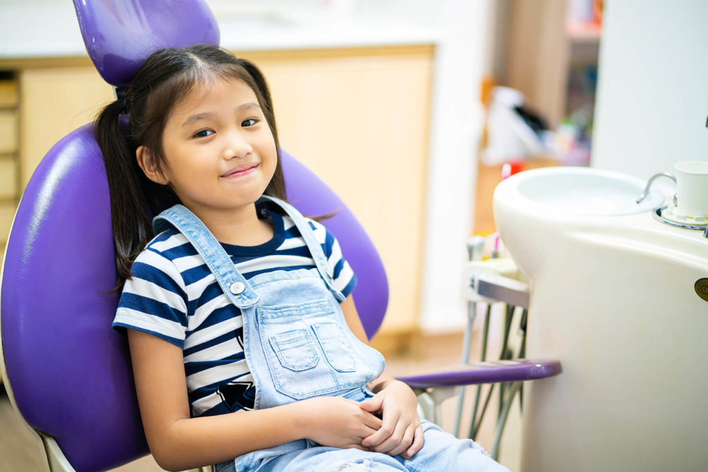 A young dental patient sits in an exam chair waiting for her checkup