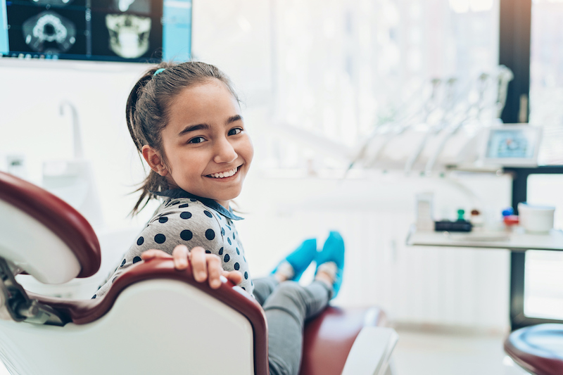 A teenage girl sits in a dental exam chair and smiles