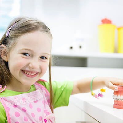 A female pediatric dentistry patient smiles and holds a model of teeth