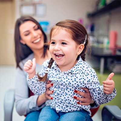 A toddler sits on her mom's lap at the dentist