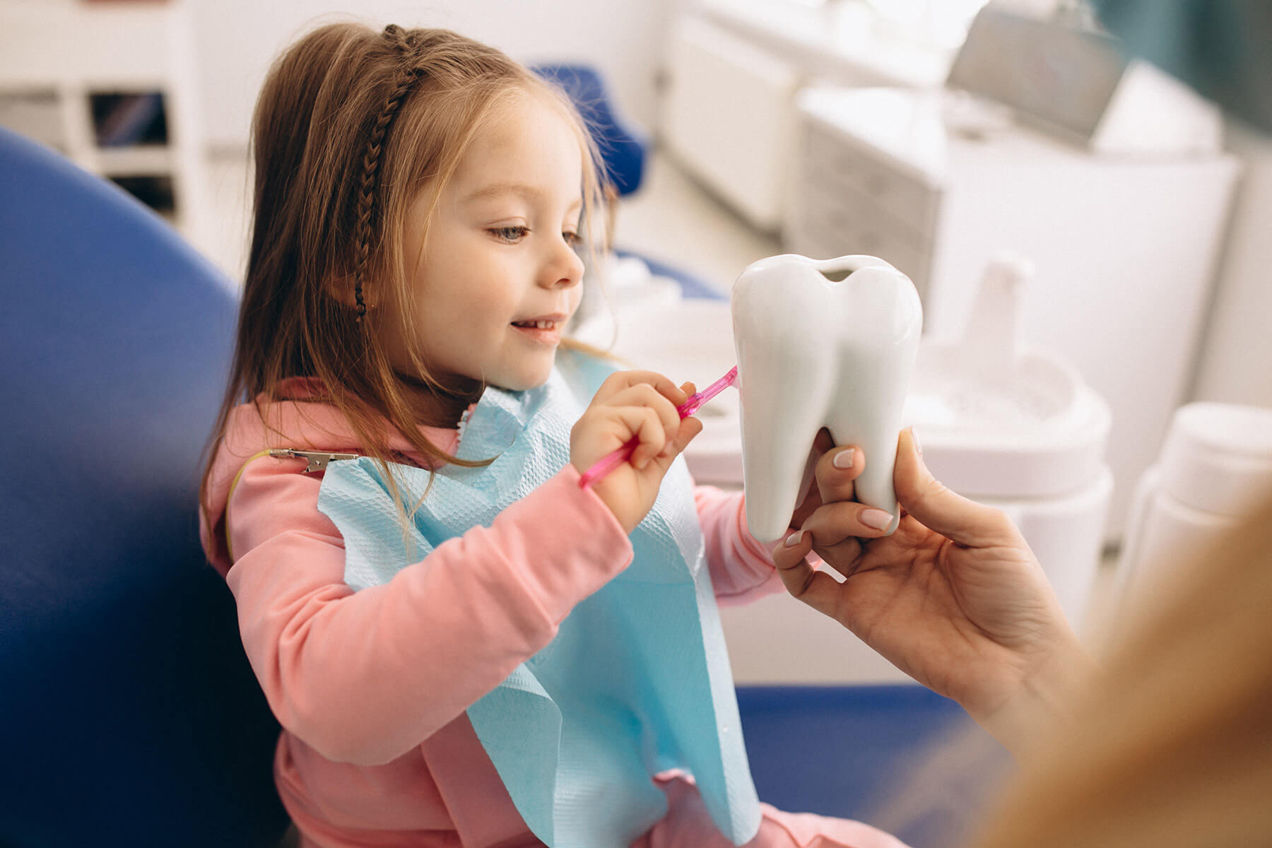 A young girl sits in a dental exam chair and learns how to brush her teeth