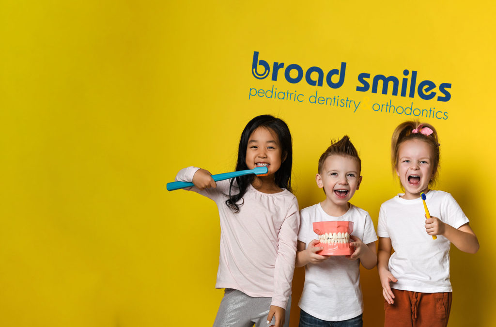 Three pediatric smiling dental patients in front of the Broad Smiles Pediatric Dentistry logo