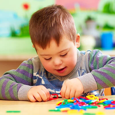 A special needs child sitting at a table playing with toys.